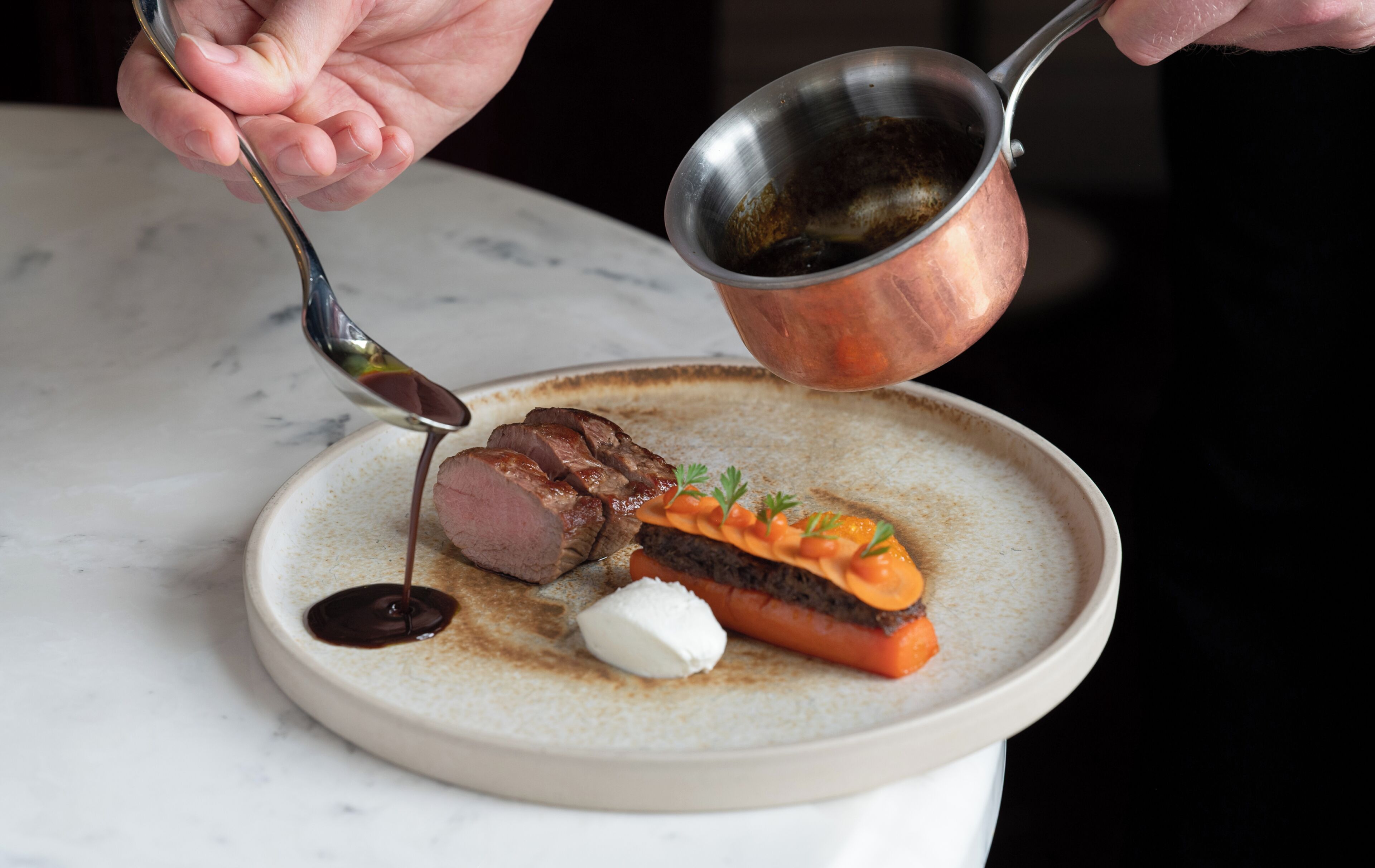 A plate with sliced meat, vegetables, and a sauce being poured.