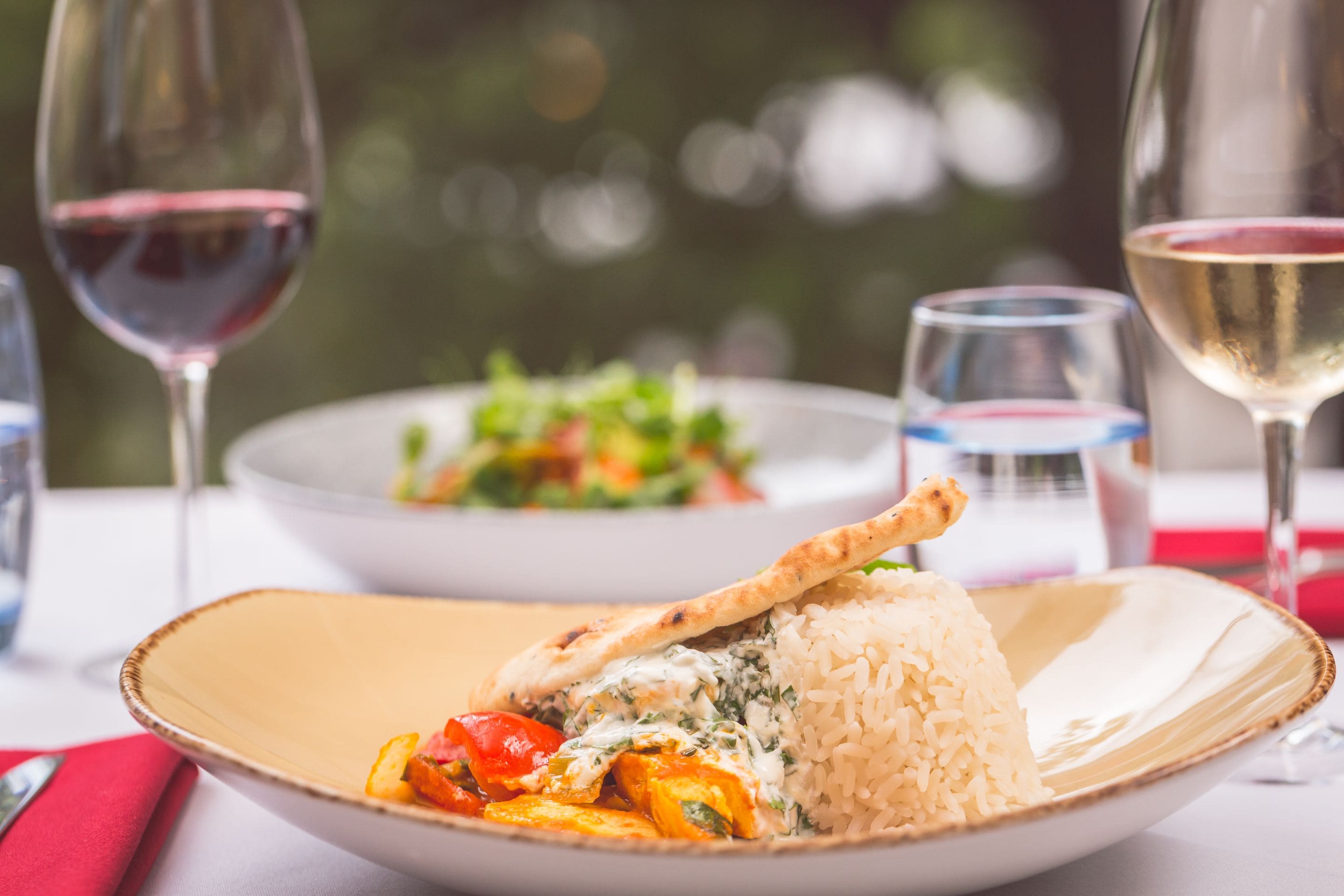 A dining table with a plate of rice and chicken, a glass of red wine, and a glass of white wine.
