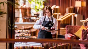 A hotel interior with a waiter serving a tray of food. The room has a cozy seating area with striped cushions and a red sofa. - Europa Hotel (Belfast)