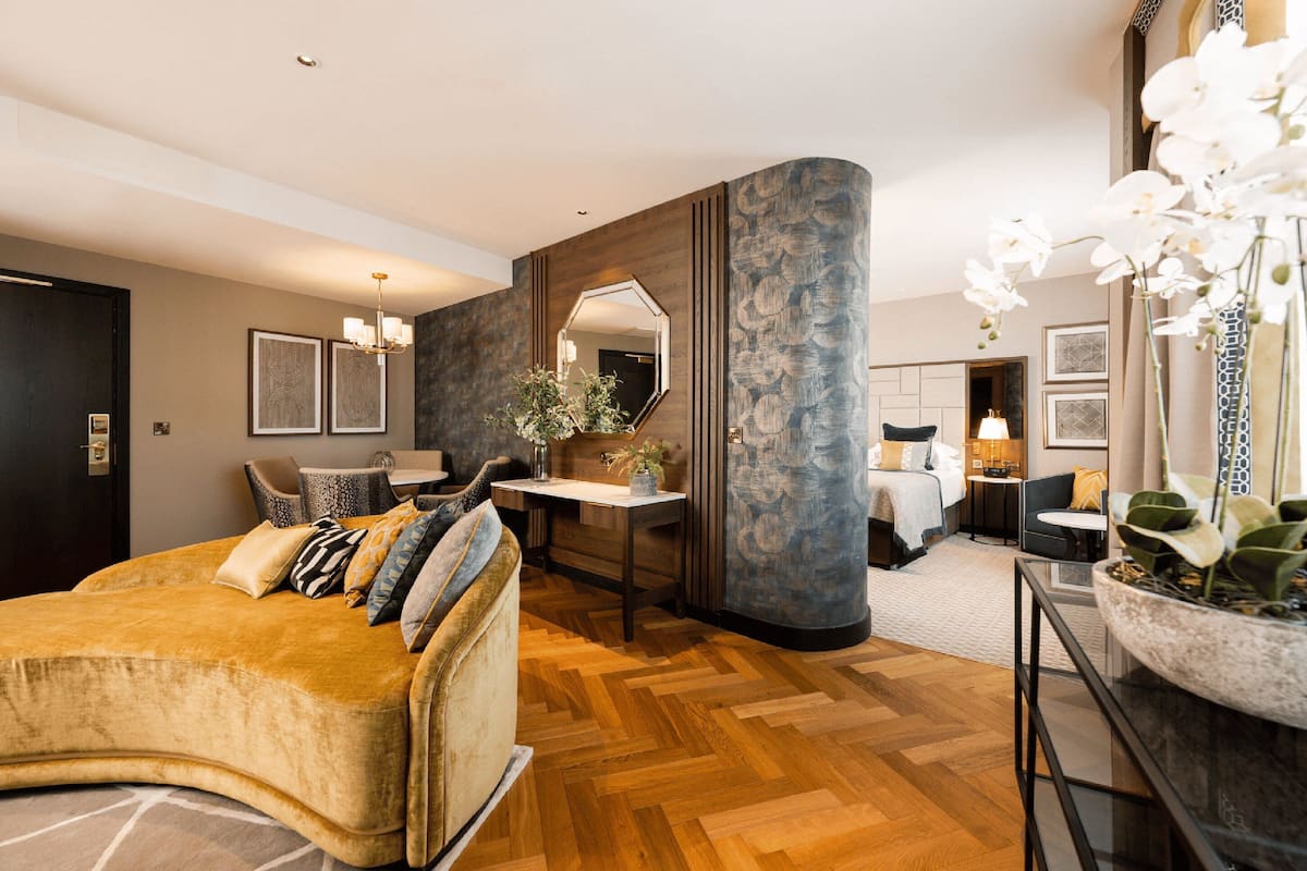 A modern hotel room with a curved sofa, a desk, a bed, and a large mirror.
