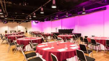 Un salón de conferencias con varias mesas redondas cubiertas con manteles rojos, sillas negras y un escenario con un atril.