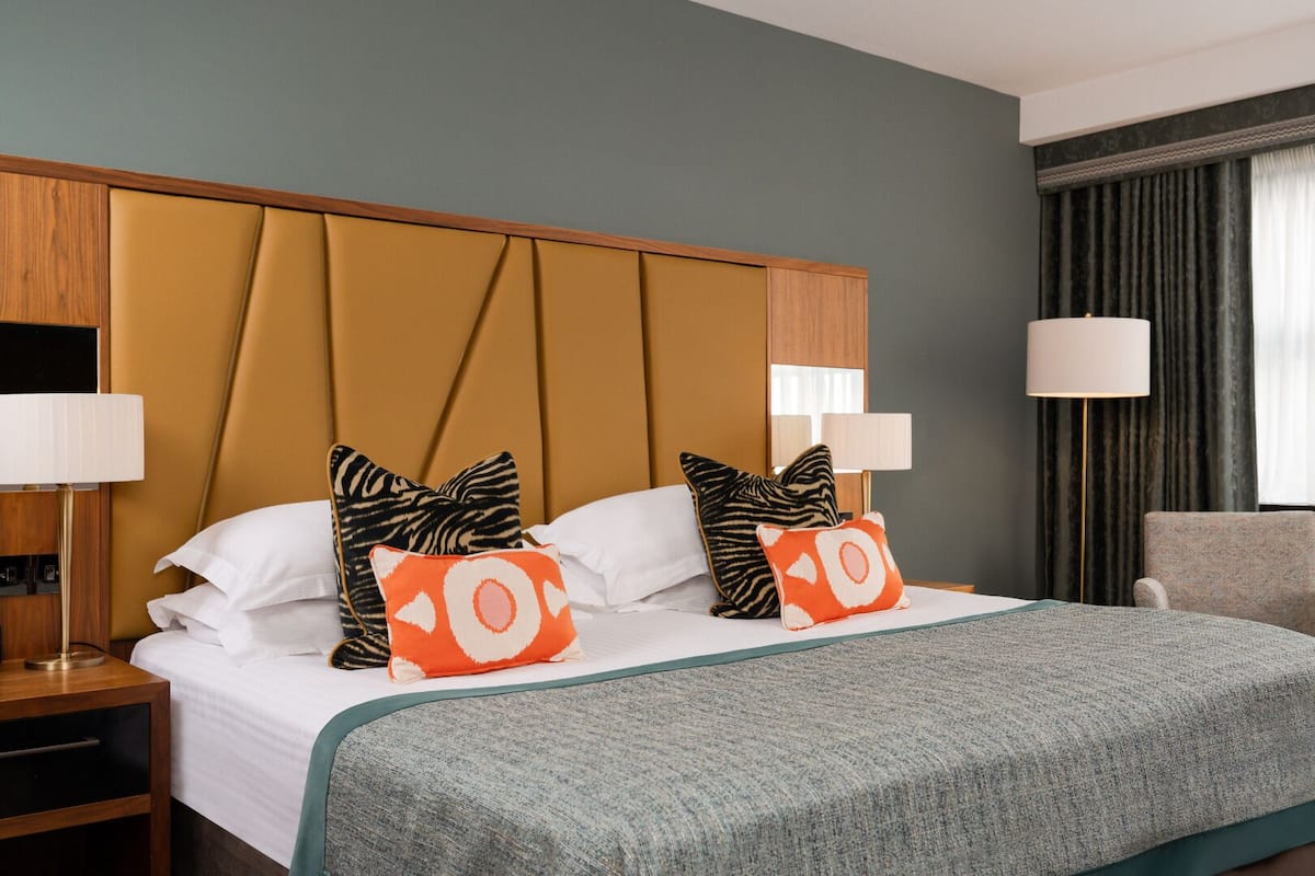 A hotel room with a large bed, two nightstands, a chair, and a window with curtains.