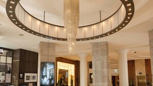 A hotel lobby with a circular chandelier, columns, a reception desk, and a black carpet with 'EUROPA BELFAST' logo. - Europa Hotel (Belfast)