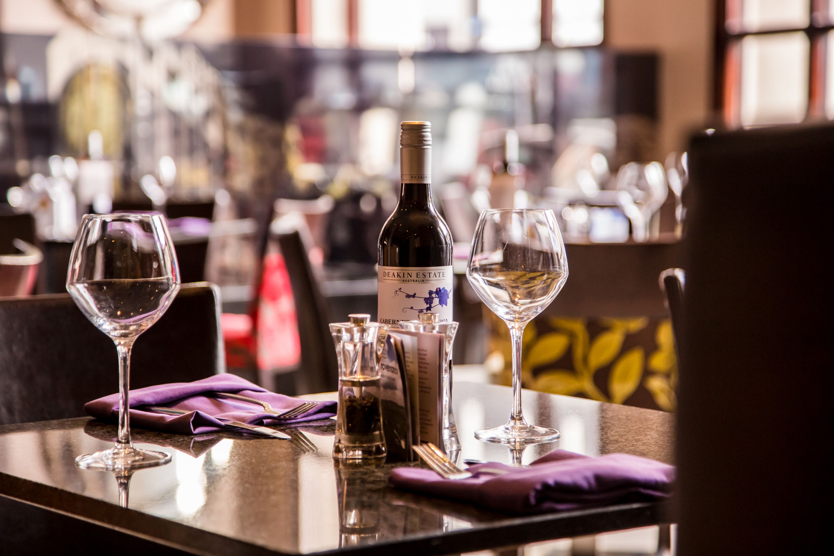 A restaurant table with a bottle of Deakin Estate wine, two wine glasses, and a menu.