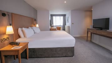 Una habitación de hotel con una cama grande, lámparas de noche, un escritorio con teléfono, televisión y vista de la habitación a través de una ventana.