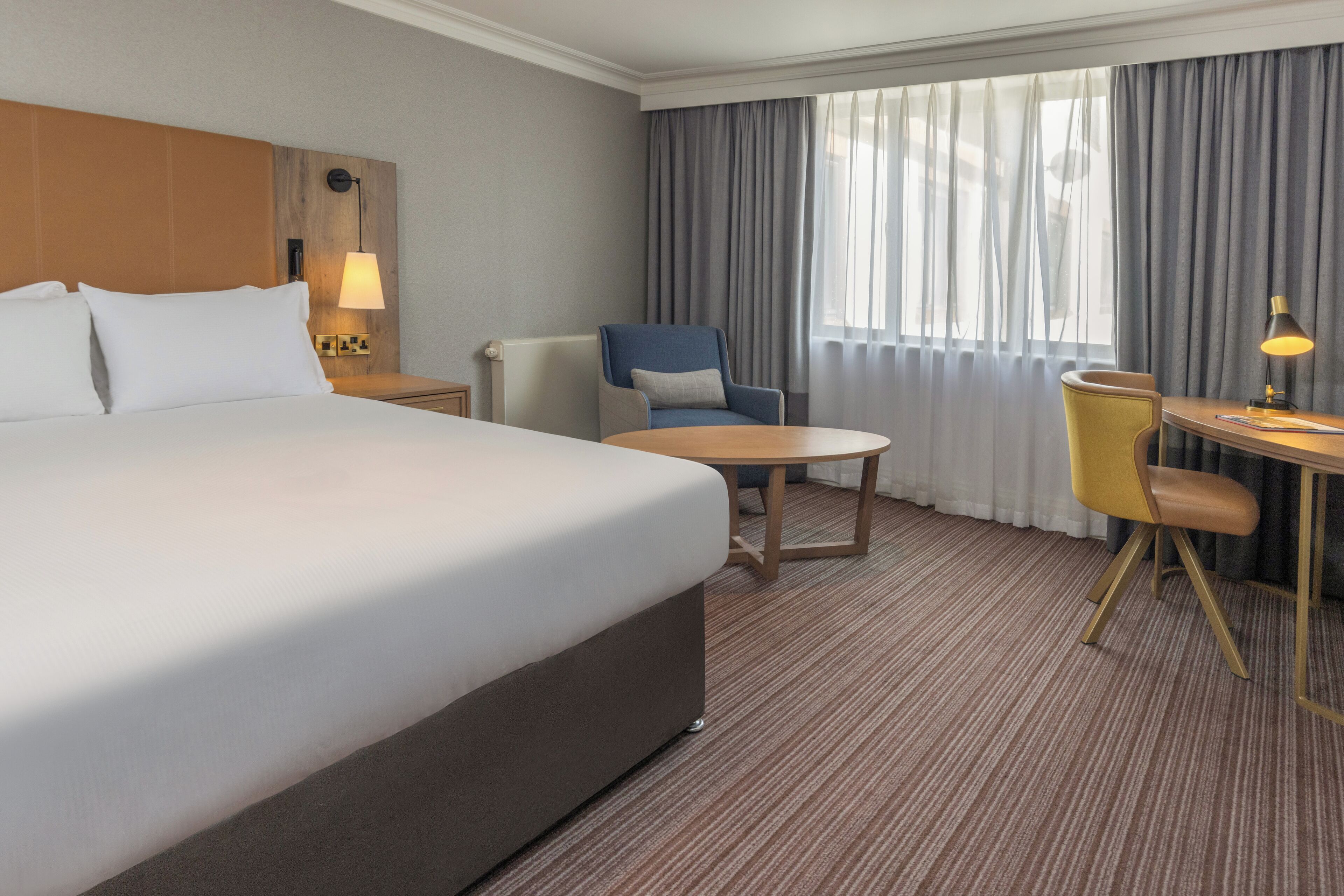 A hotel room with a large bed, a desk, a chair, and a window with curtains.