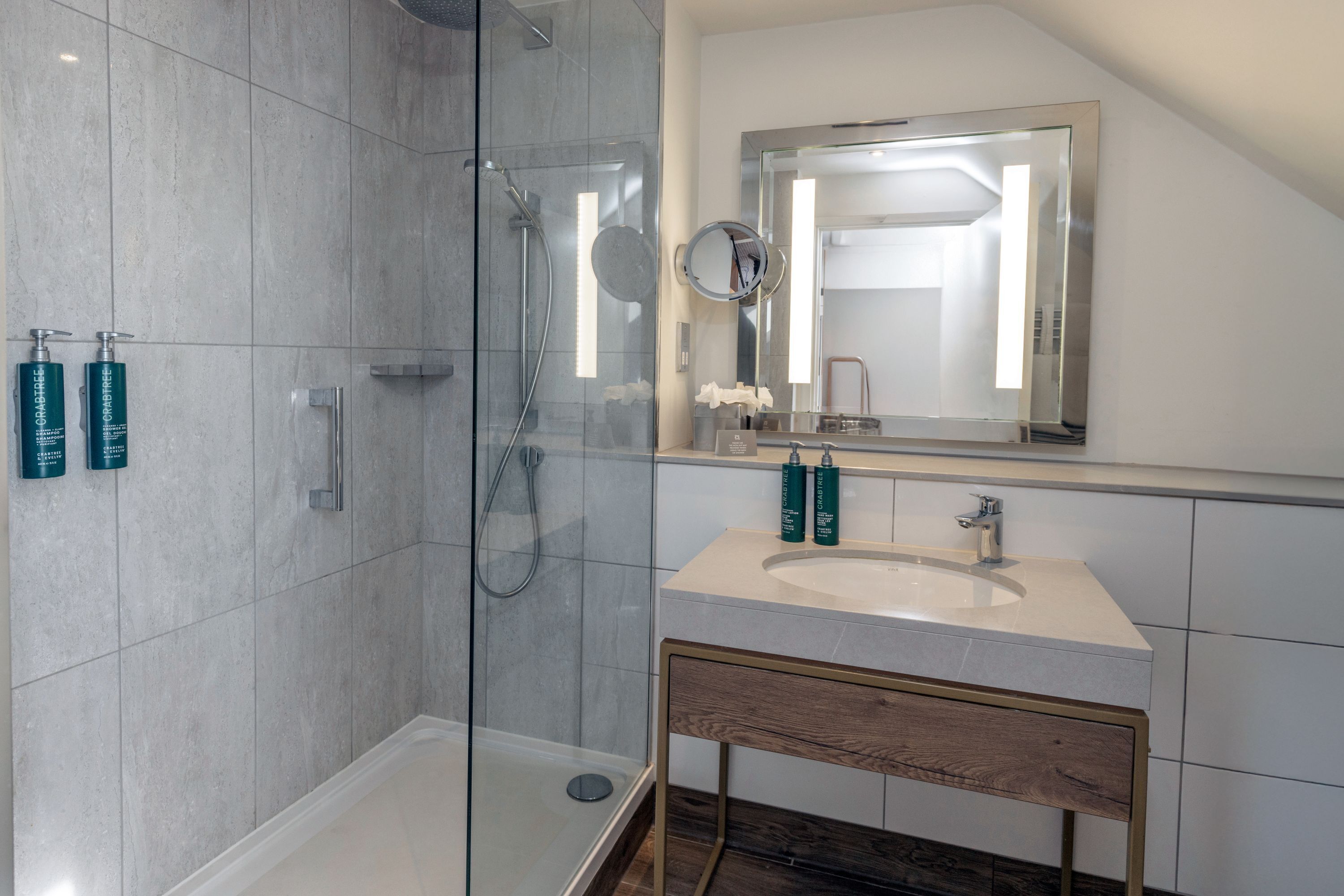 Un baño moderno con ducha de vidrio, un lavabo con espejo y artículos de aseo en la pared.