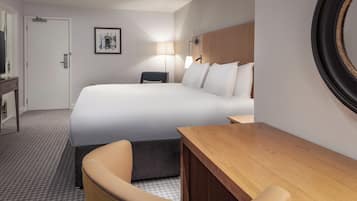 A hotel room with a large bed, a desk, a chair, a lamp, and a framed picture on the wall.