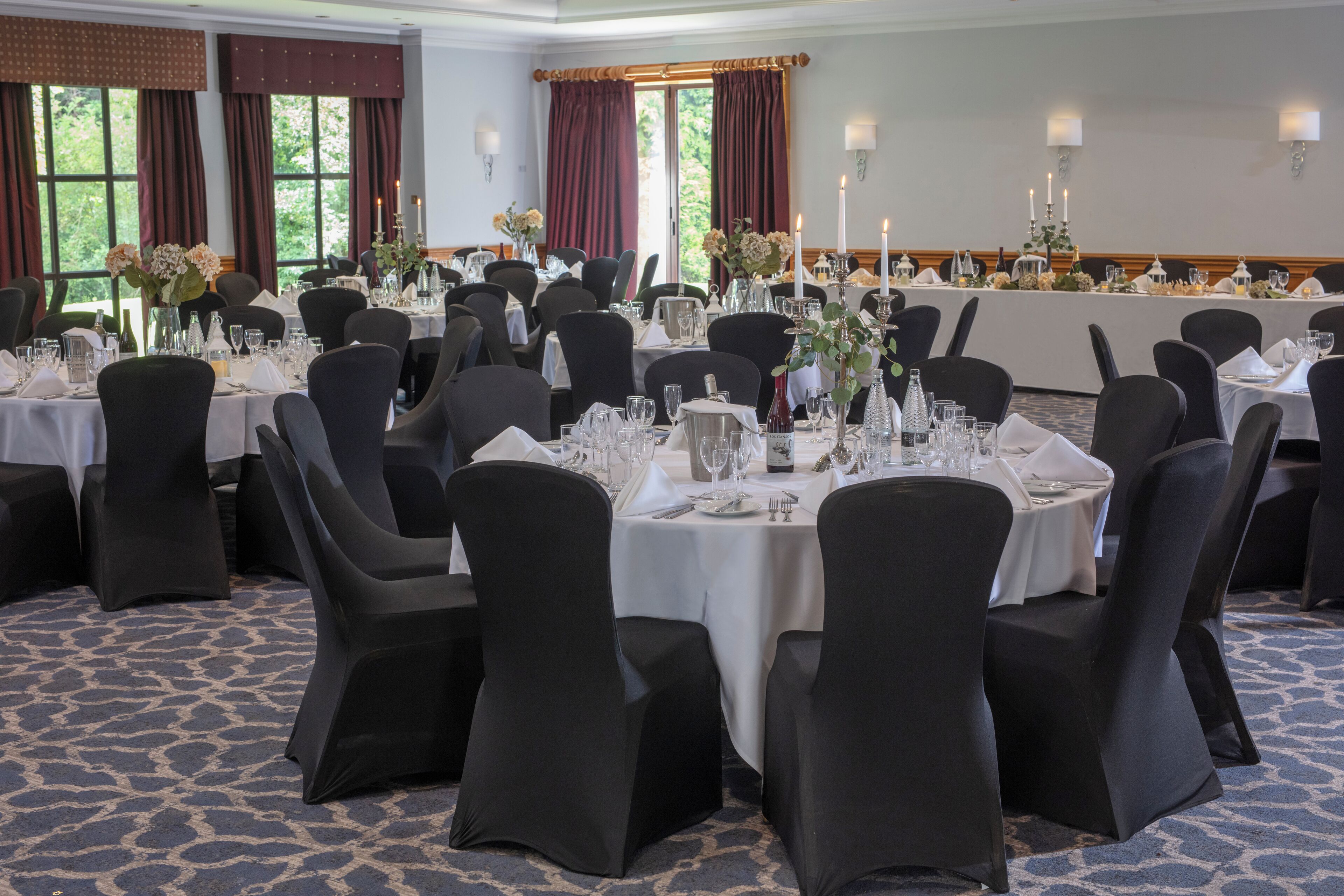 A banquet hall with round tables set for dining, black chairs, and white tablecloths.