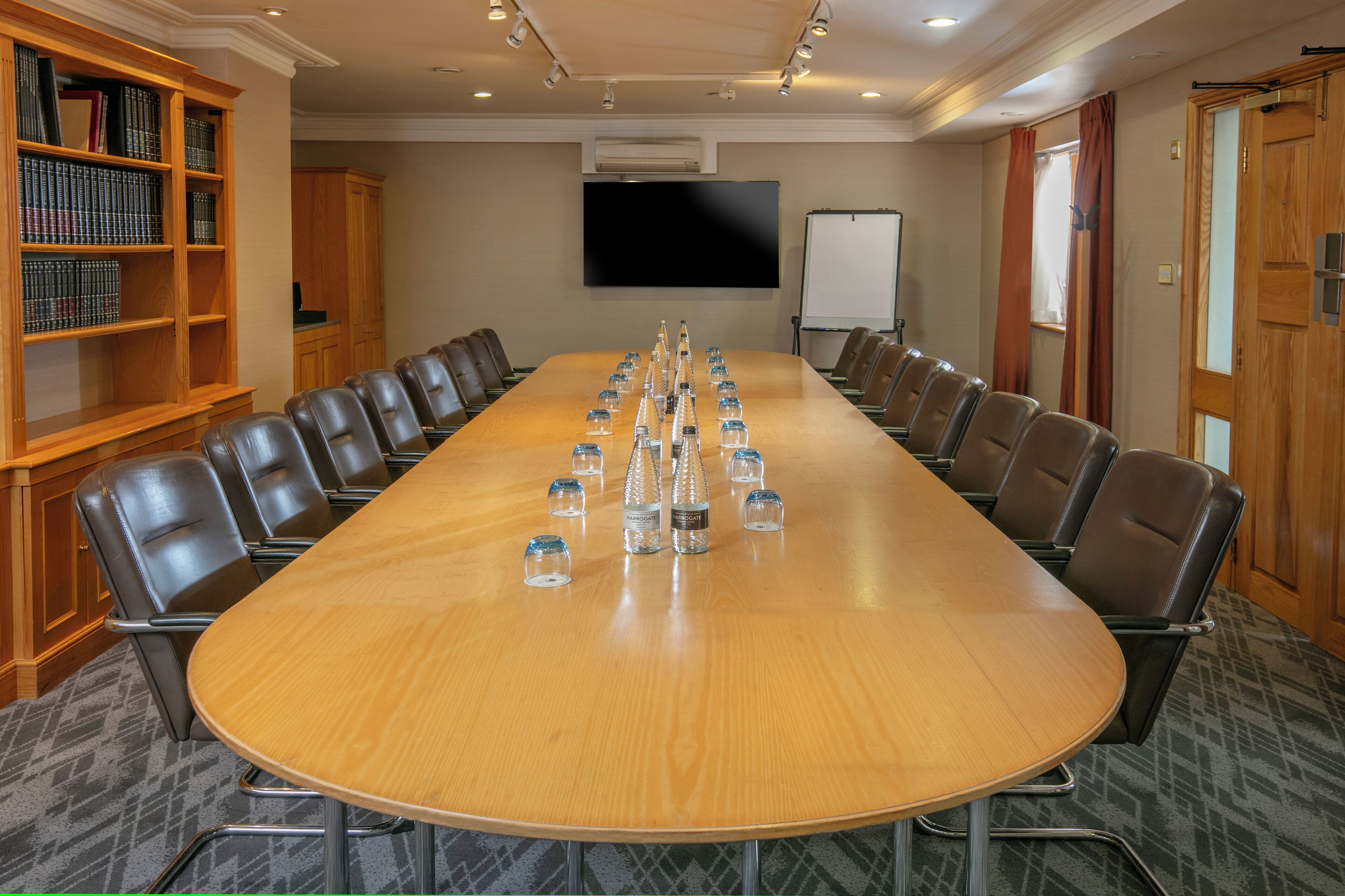 A conference room with a long table, chairs, a bookshelf, a TV, and a whiteboard.