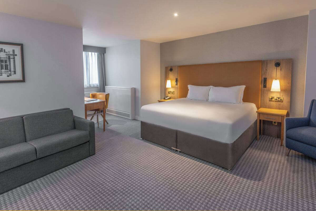 A hotel room with a large bed, a sofa, a desk, and a chair.
