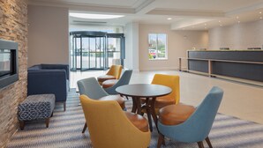 Un hall d’entrée moderne avec un mur d’accent en pierre, une table ronde entourée de chaises, un espace salon avec des canapés et un comptoir d’accueil.