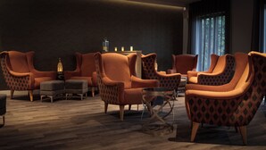 Un salon moderne avec plusieurs fauteuils orange, une petite table ronde et un pouf à motifs.