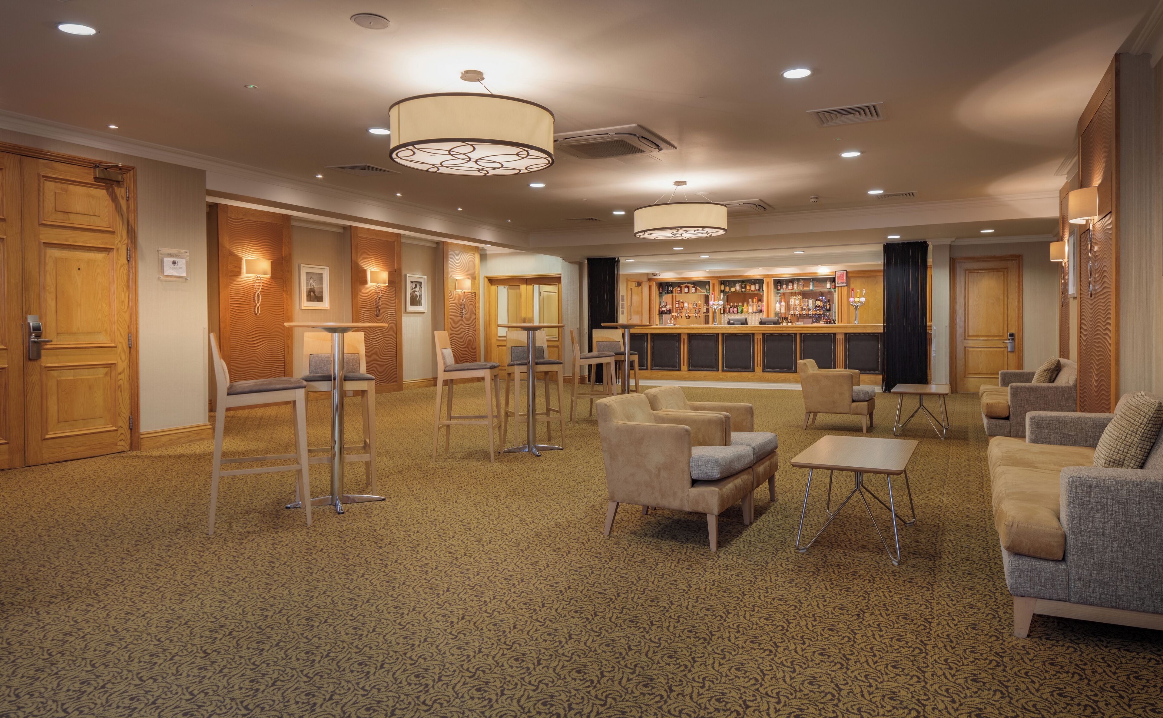 A hotel lobby with a bar area, seating arrangements, and a patterned carpet.