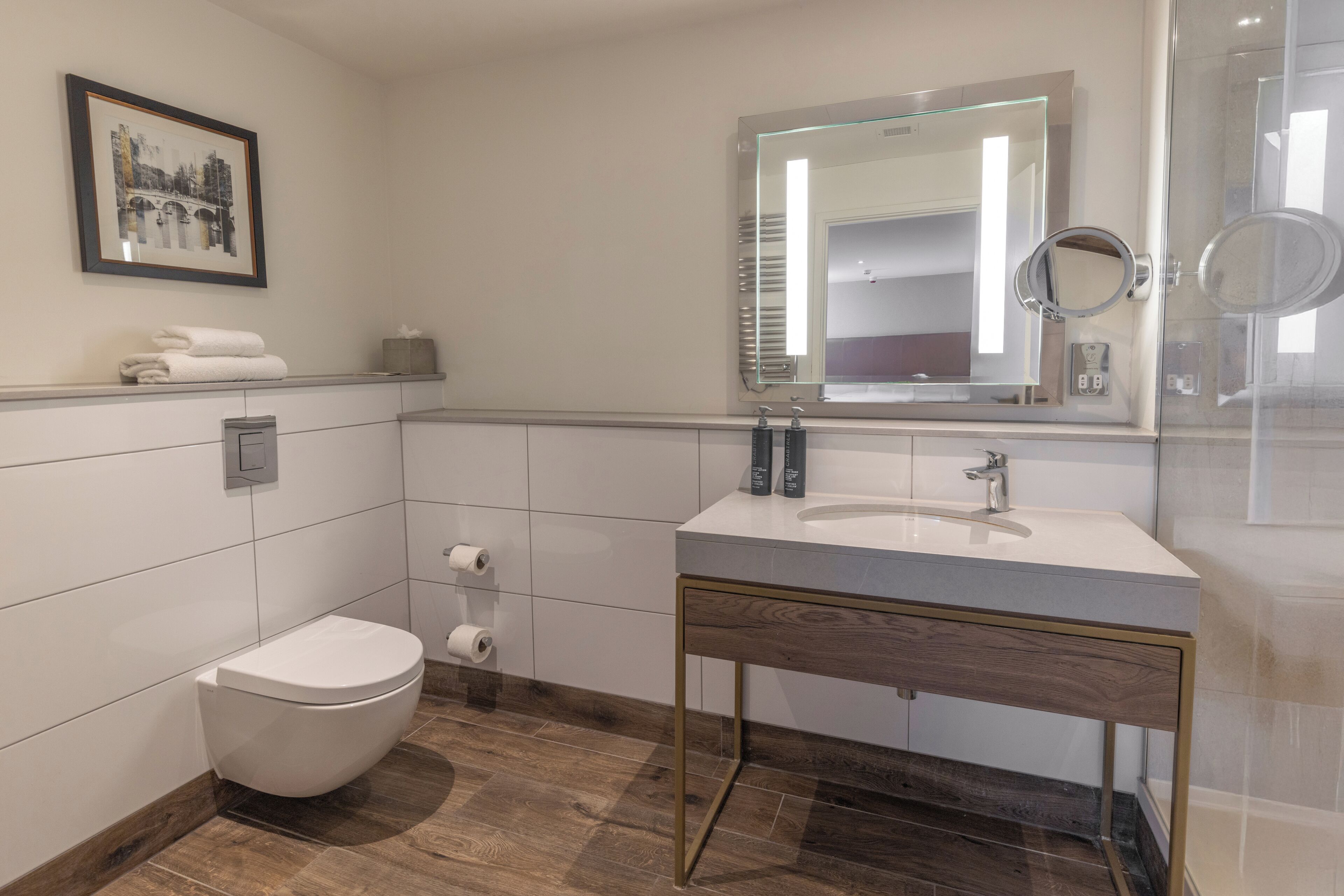 A modern bathroom with a white toilet, a sink with a mirror, and a framed picture on the wall.