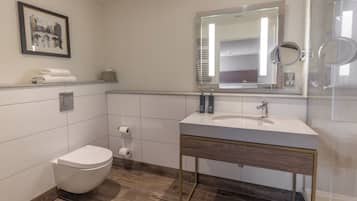 A modern bathroom with a white toilet, a sink with a mirror, and a framed picture on the wall.