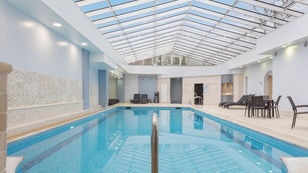 Une piscine intérieure dotée d’un toit en verre, de murs carrelés et d’espaces aménagés pour s’asseoir.
