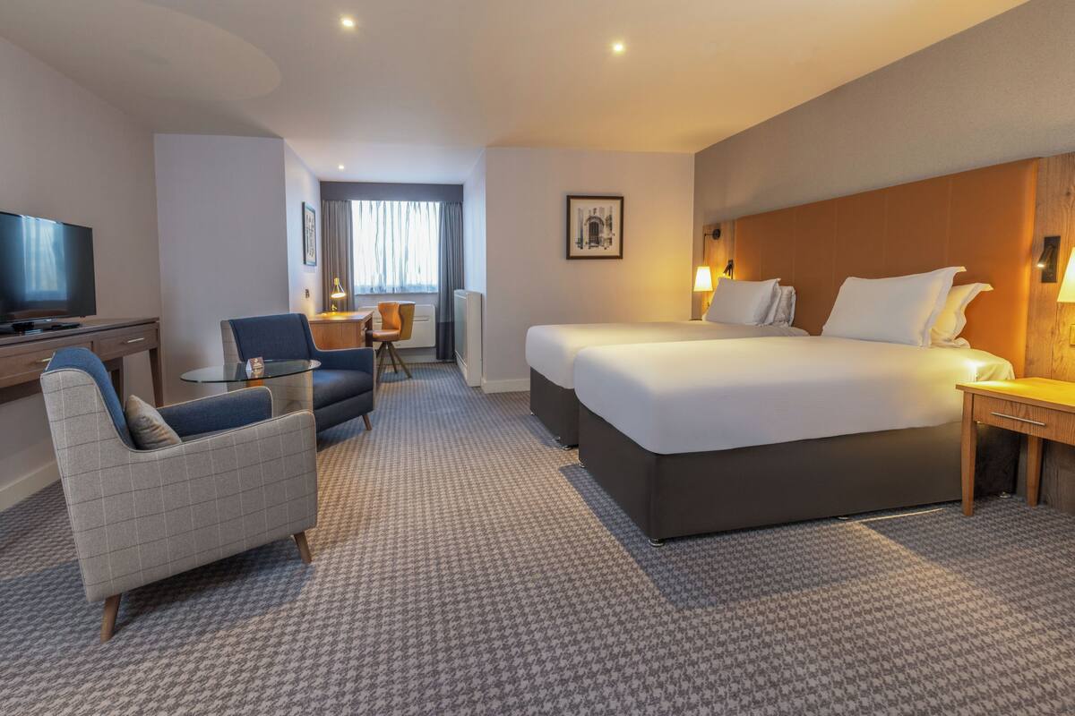 A hotel room with a large bed, a desk, a chair, a TV, and a small table.