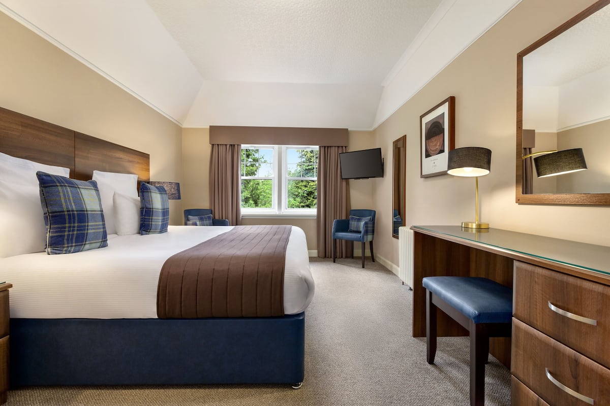 Une chambre d’hôtel avec un grand lit, un bureau, une chaise, une télévision et une fenêtre avec des rideaux.