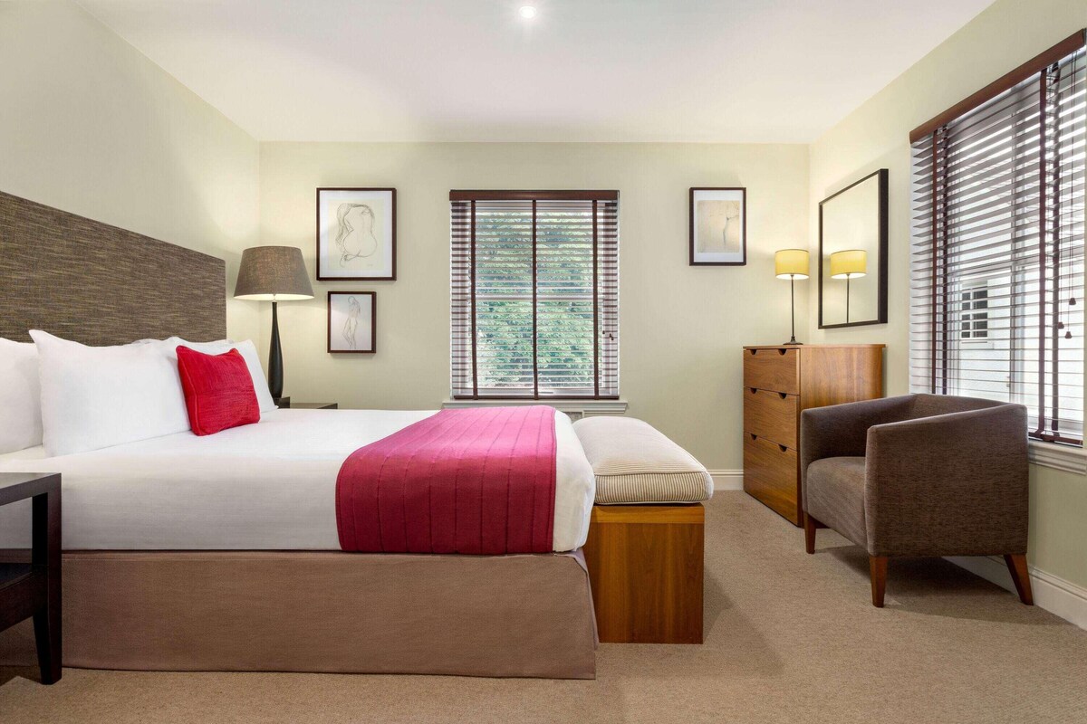 Een hotelkamer met een bed, nachtkastjes, een stoel, een kaptafel en een raam met jaloezieën.