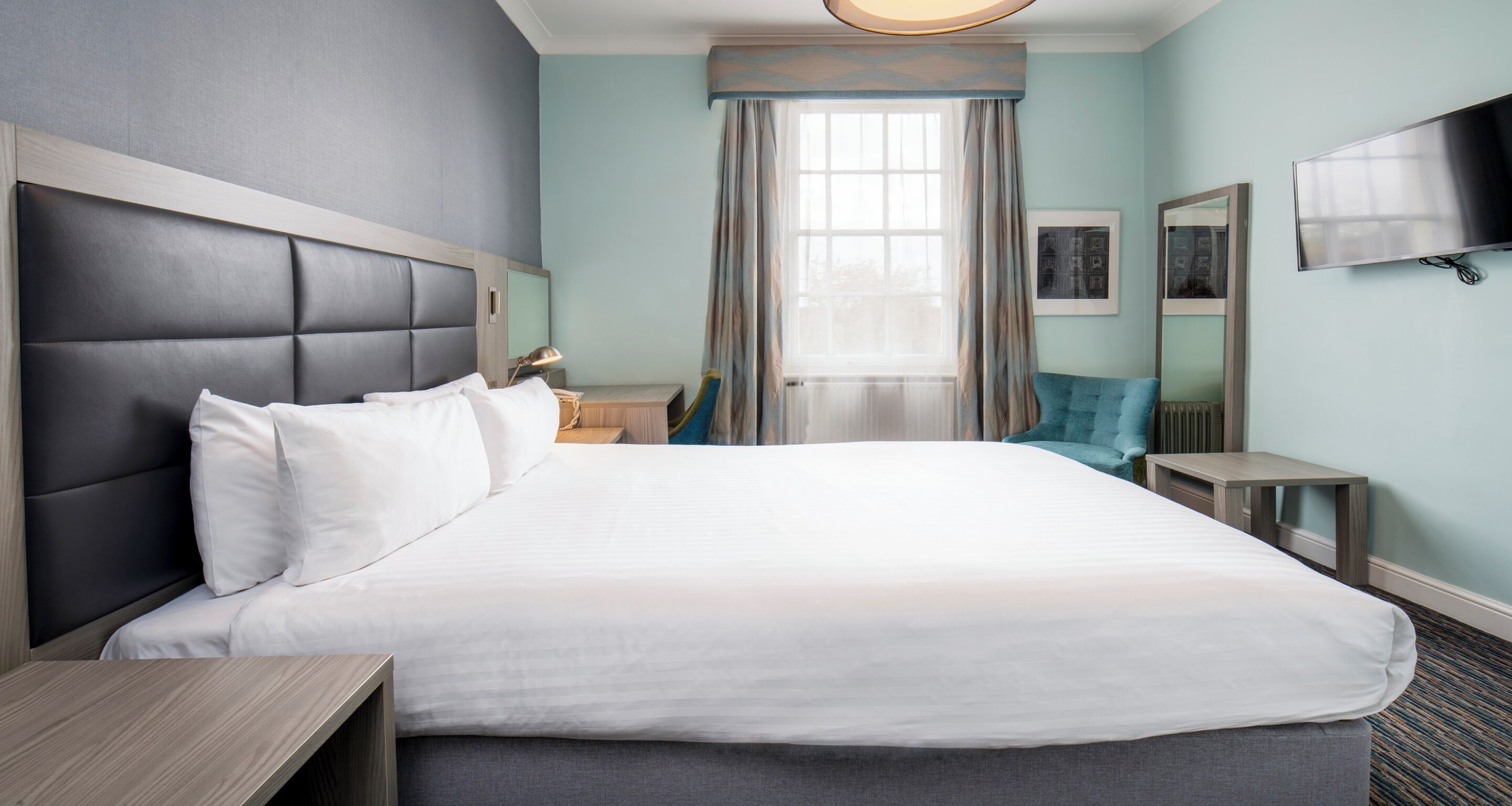 A hotel room with a large bed, a flat-screen TV, a desk, and a window with curtains.