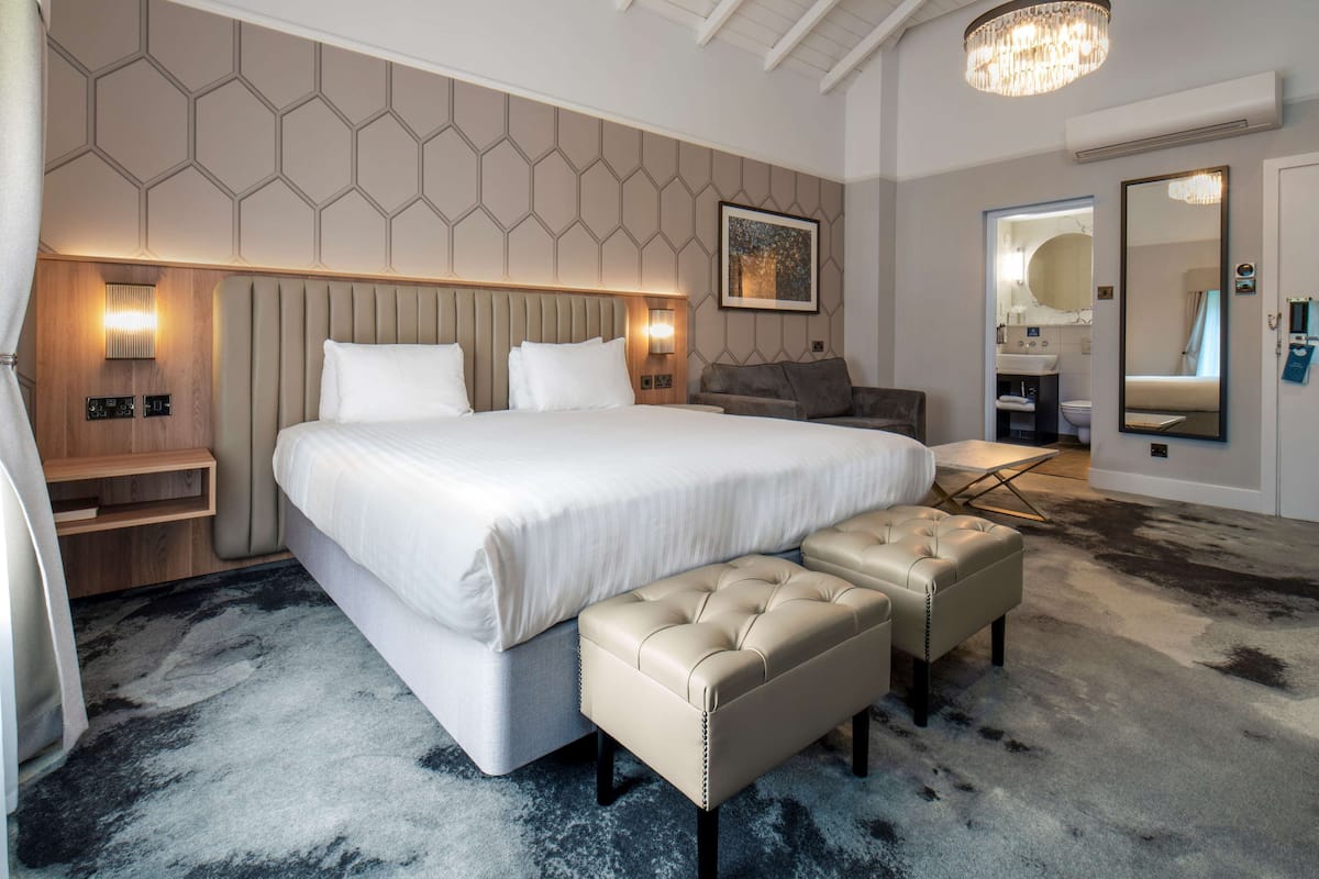A modern hotel room with a large bed, a seating area, and a bathroom visible through an open door.