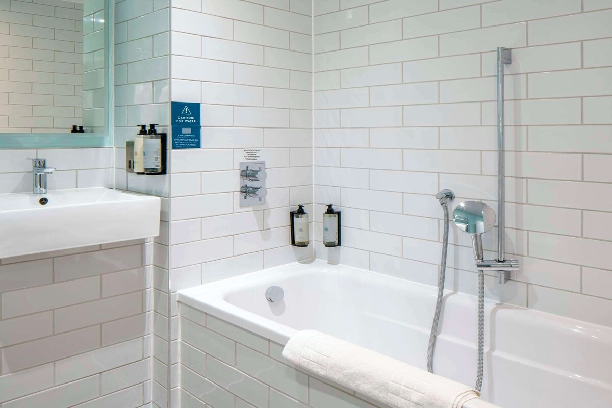 A modern bathroom with white tiles, a sink, a bathtub, and a shower.