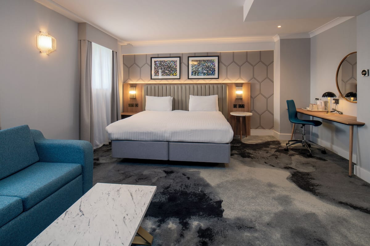 A hotel room with a bed, a desk, a chair, a sofa, and a coffee table.
