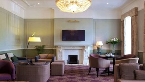 A spacious living room with a fireplace, comfortable seating, a television, and a chandelier. - London Chigwell Prince Regent Hotel, BW Signature Collection (Woodford Green)