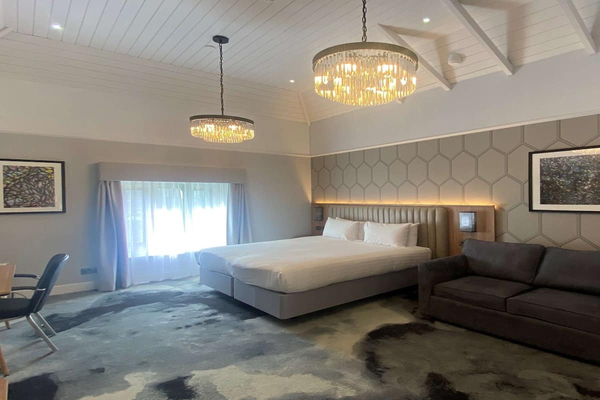 A modern hotel room with a large bed, a sofa, and two pendant lights.