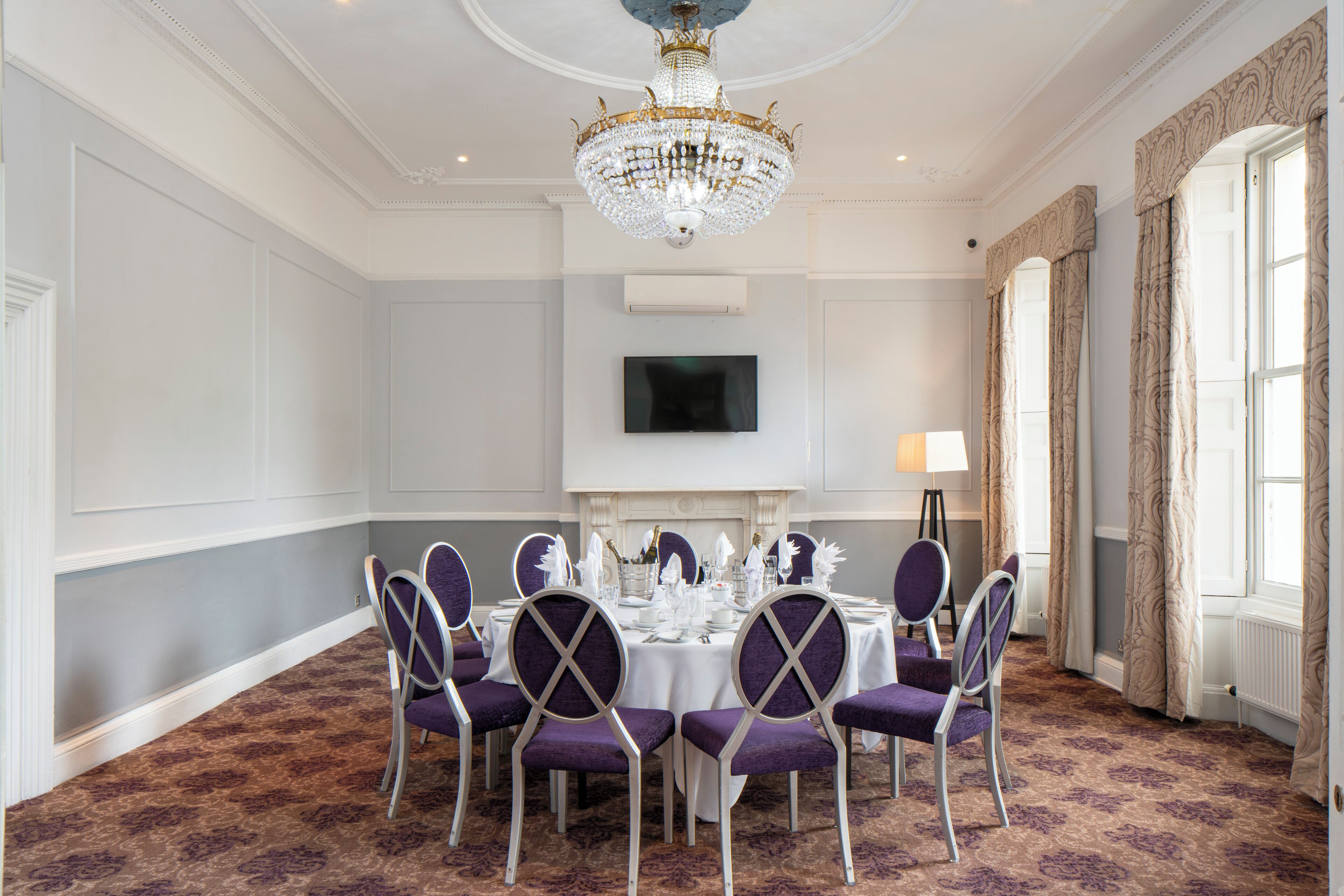 A formal dining room with a chandelier, a television, and a fireplace.