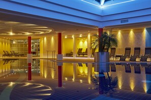 Un área de piscina interior moderna con una barrera de vidrio, sillas de descanso y una piscina reflectante.