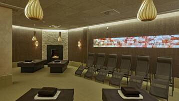 Une salle de spa équipée d’une cheminée, de tables de massage et d’un grand écran fixé au mur.