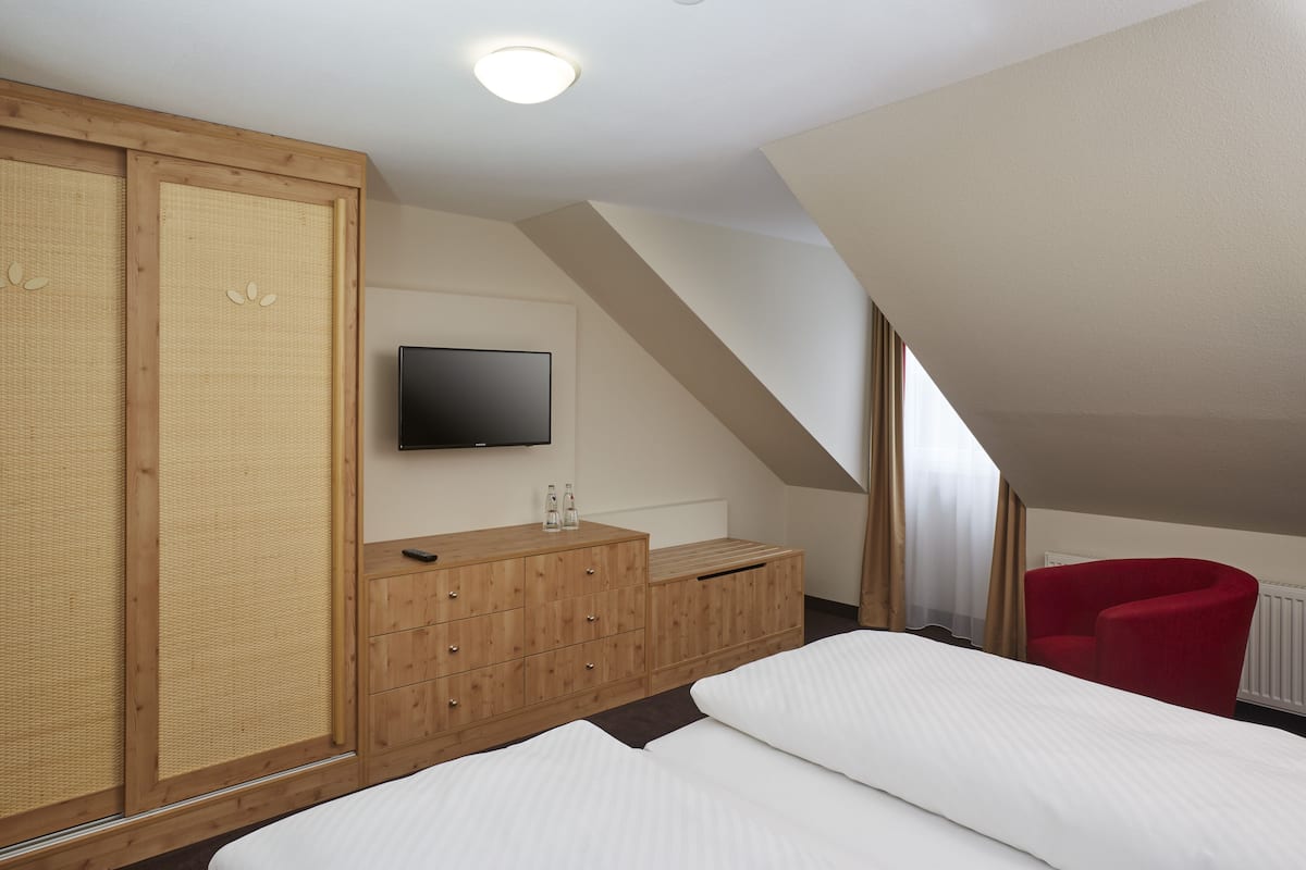 A bedroom with a bed, wooden wardrobe, a television, and a red chair.
