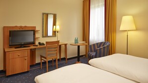 Een hotelkamer met een bed, een bureau met een televisie, een stoel, een klein tafeltje met twee flessen en een lamp.