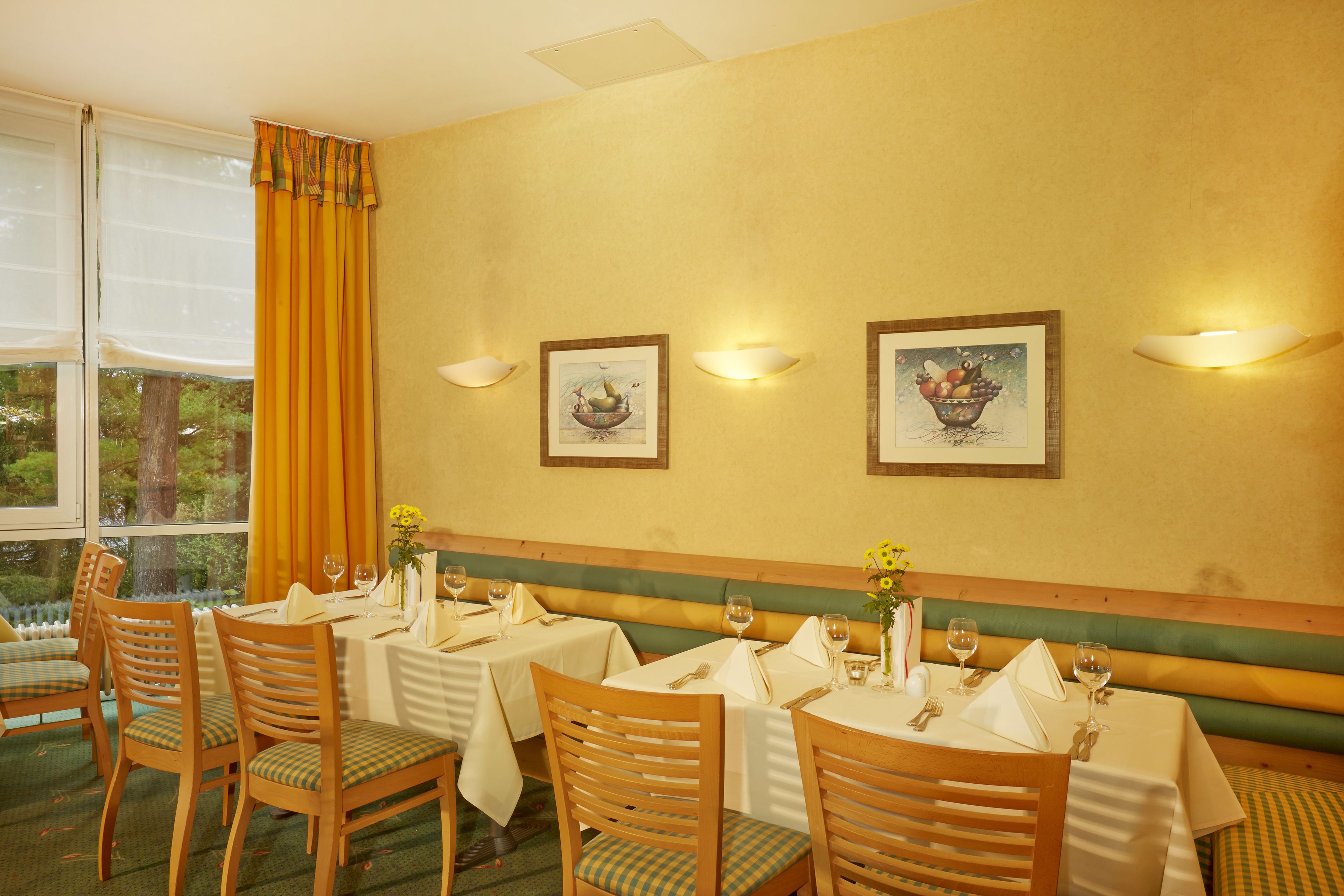 Un espace repas avec des tables préparées pour deux personnes, des chaises en bois et des luminaires fixés au mur.