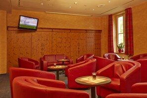 A hotel room with red leather chairs, a television mounted on the wall, and a window with plaid curtains.