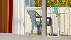 Een balkon met een tafel en stoelen, uitzicht op bomen, en een hekwerk.