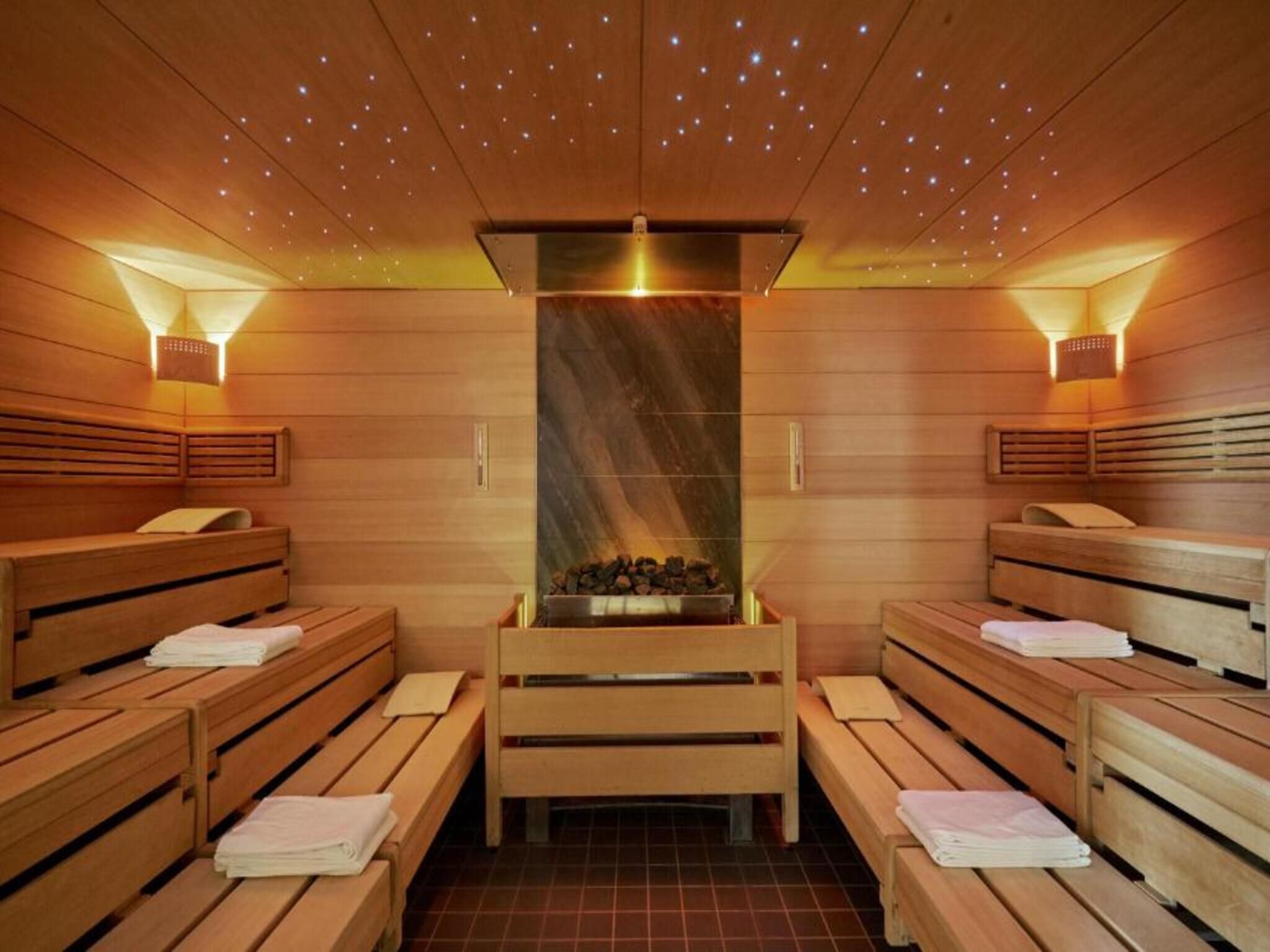 A sauna room with wooden benches and a central fire feature.