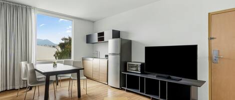 A modern living room with a dining table, sofa, TV, and kitchen area.