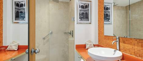 Une salle de bain moderne avec une douche à parois de verre, un lavabo blanc et deux tableaux encadrés accrochés aux murs.