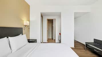 A hotel room with a bed, bedside table, lamp, and a view into the bathroom.