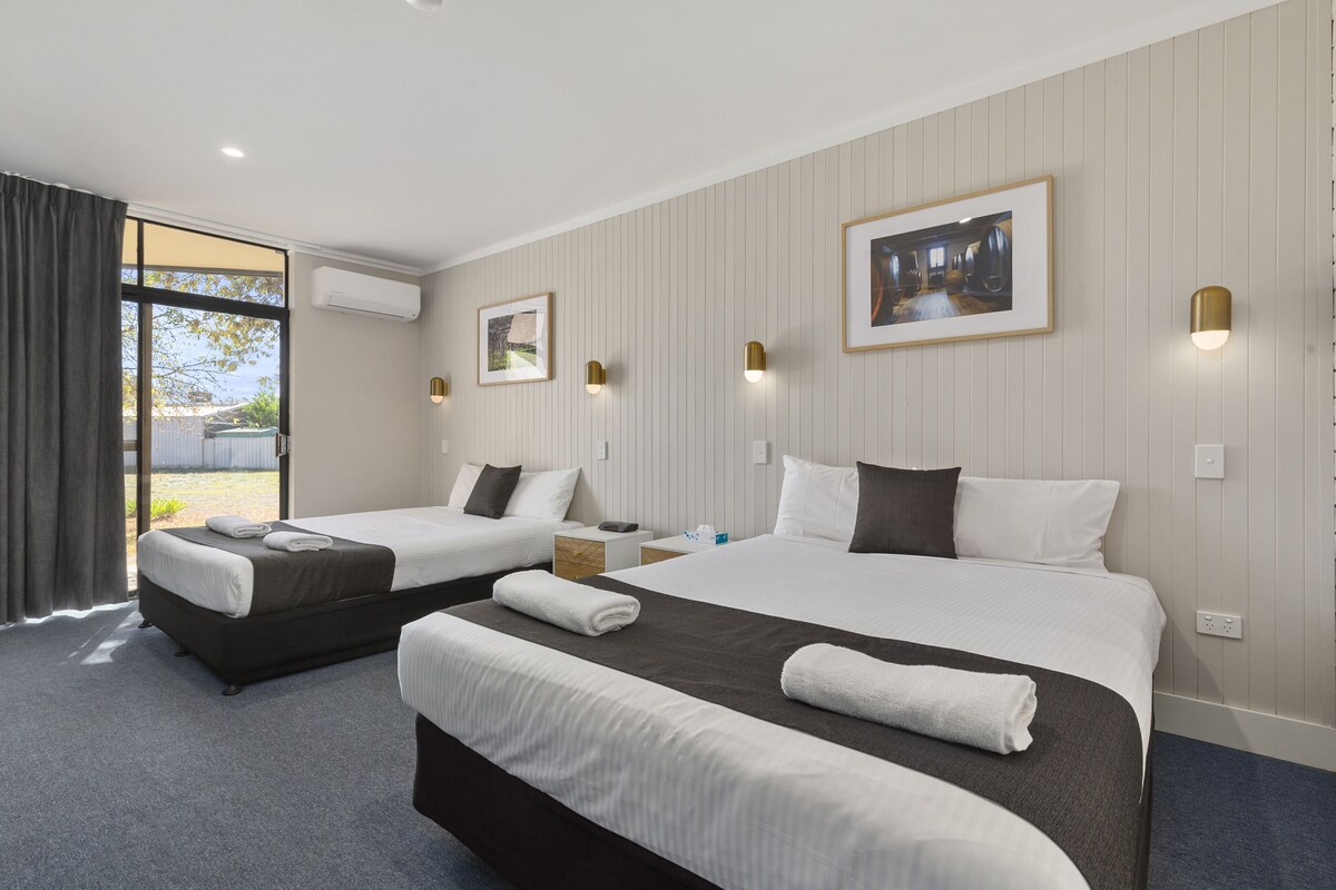 A hotel room with two beds, a large window, and a framed picture on the wall.