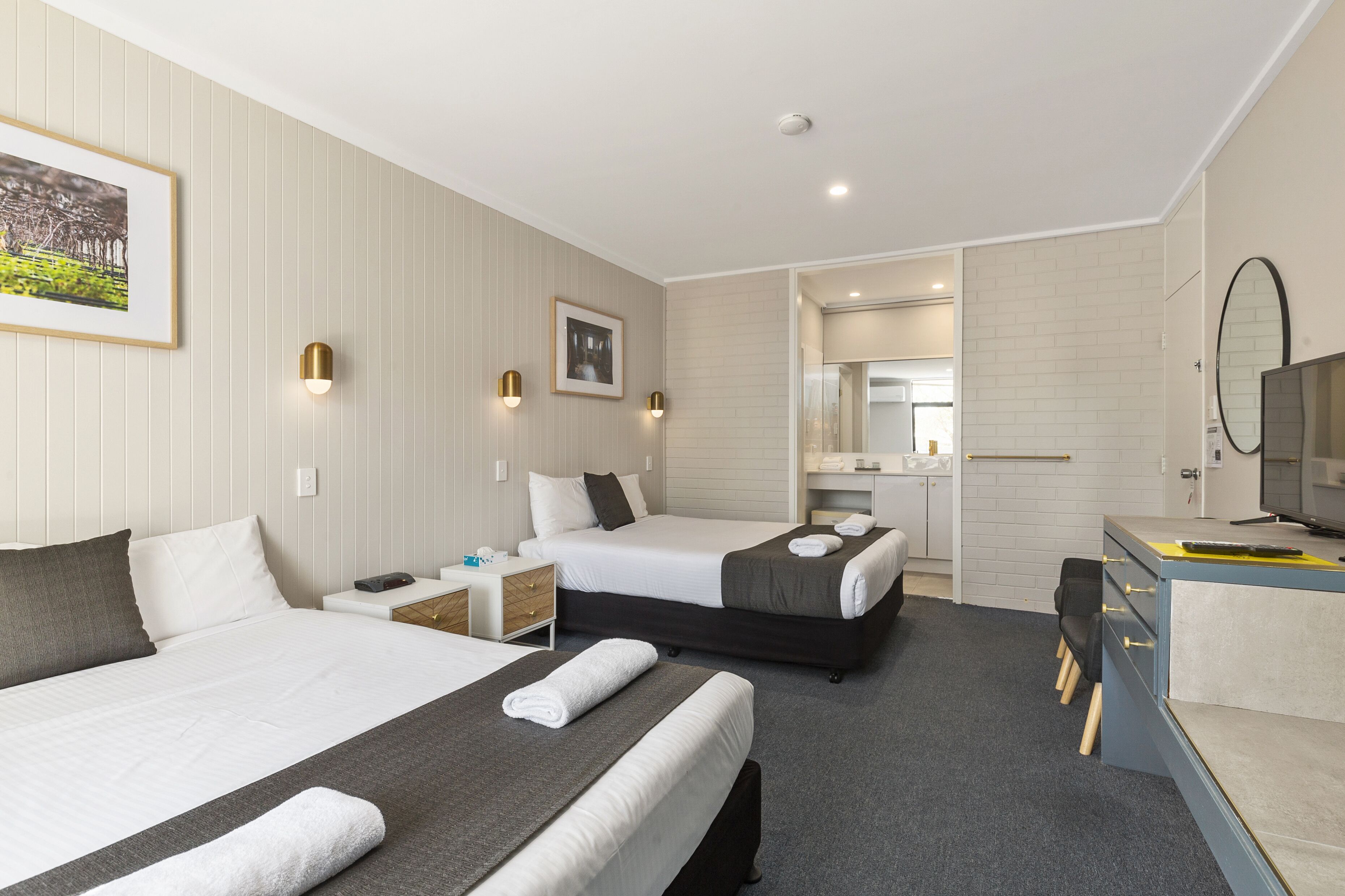 Habitación de hotel con dos camas, un escritorio, una silla, un espejo y un televisor.