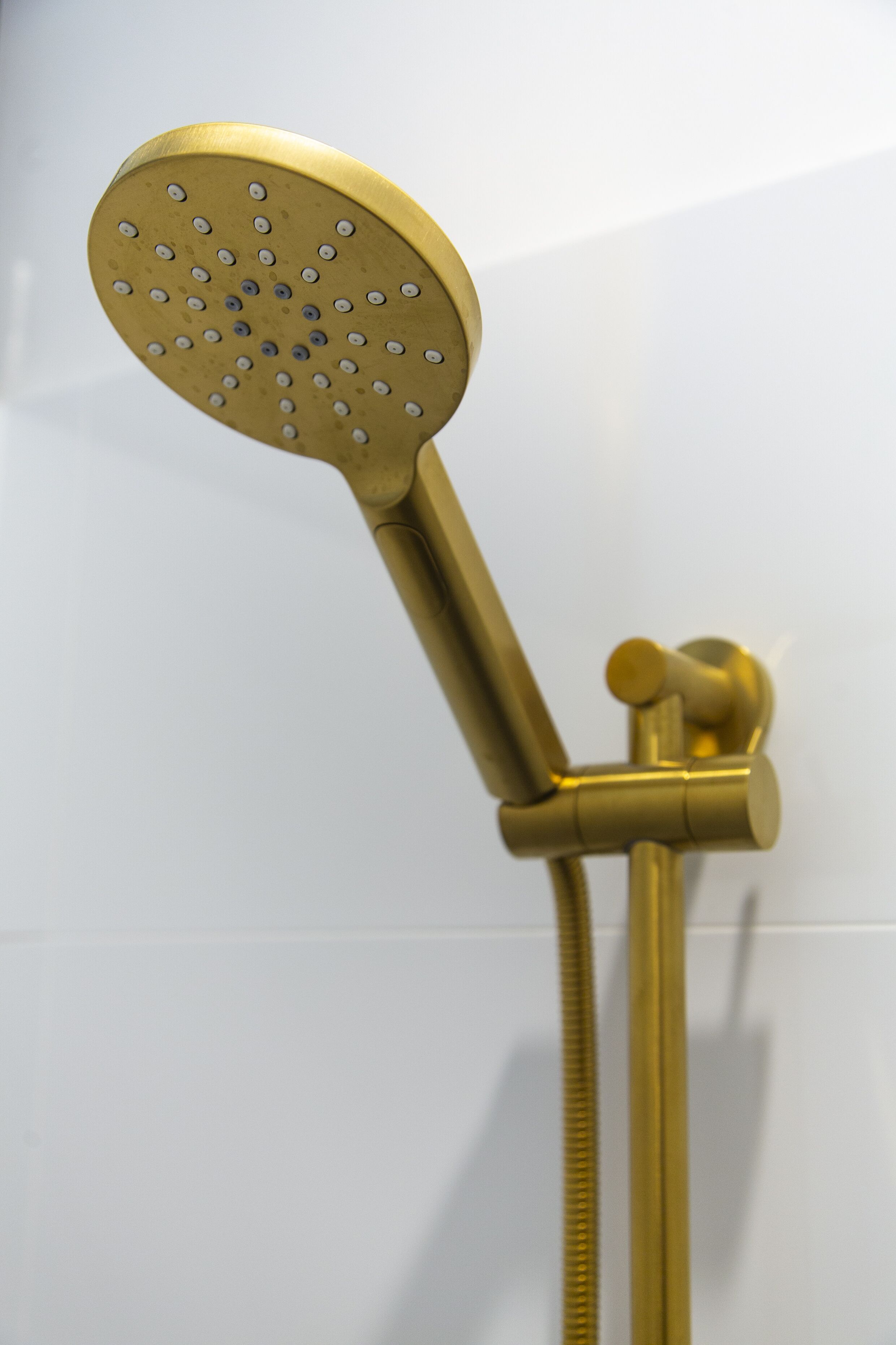 Un soffione dorato dal design rotondo e con più ugelli, collegato a un tubo verticale tramite un tubo flessibile.