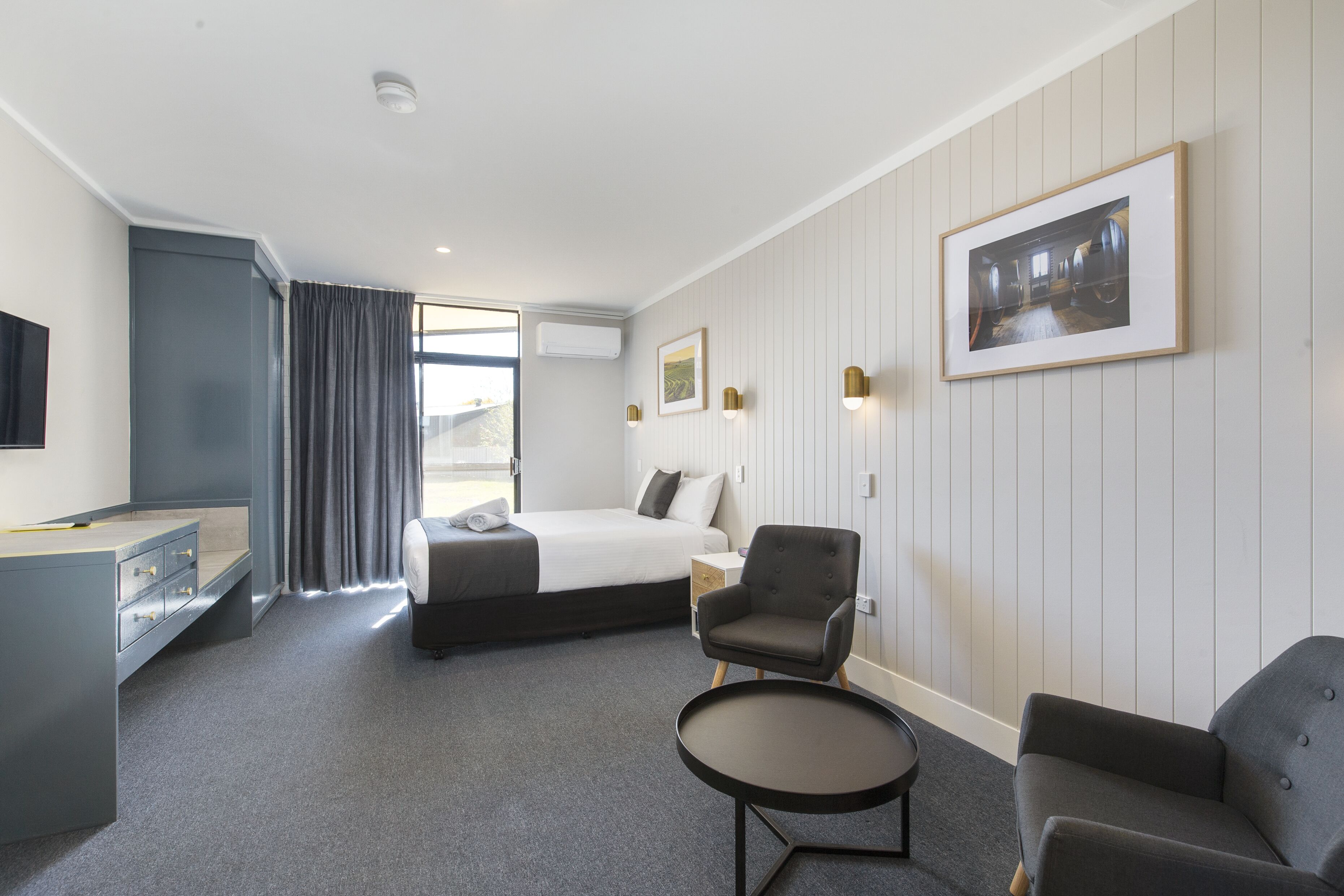 A hotel room with a bed, two armchairs, a small table, a desk, and a TV.