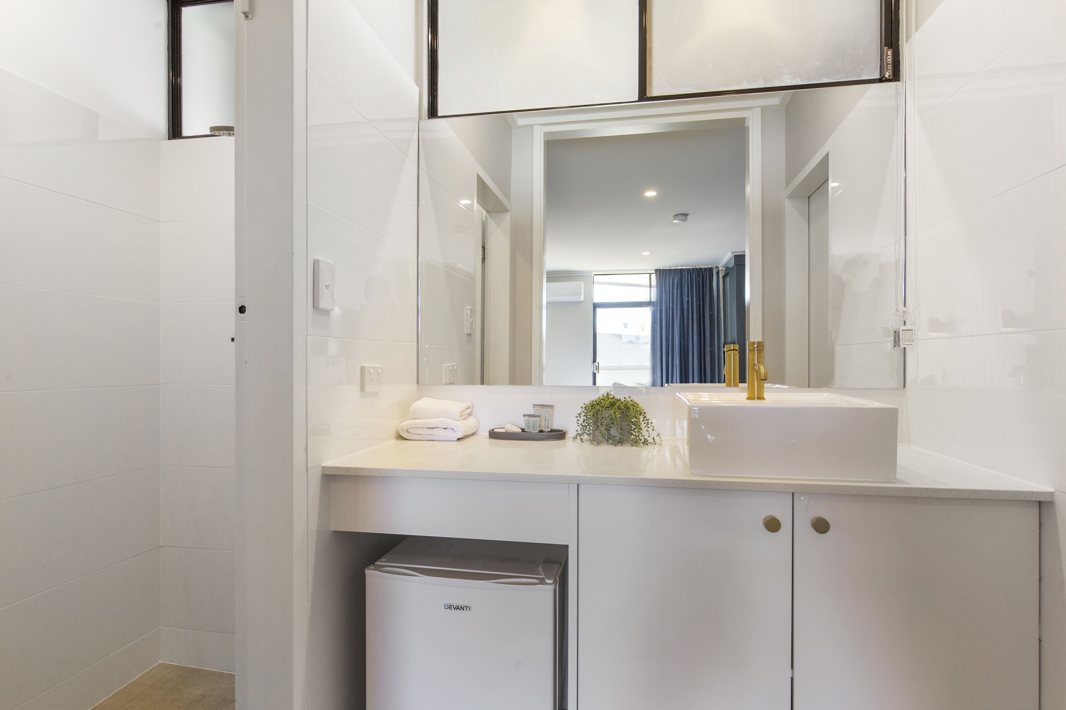 Een moderne badkamer met witte tegels, een ingebouwd wastafelmeubel, een spiegel en een compact wit apparaat onder het aanrecht.