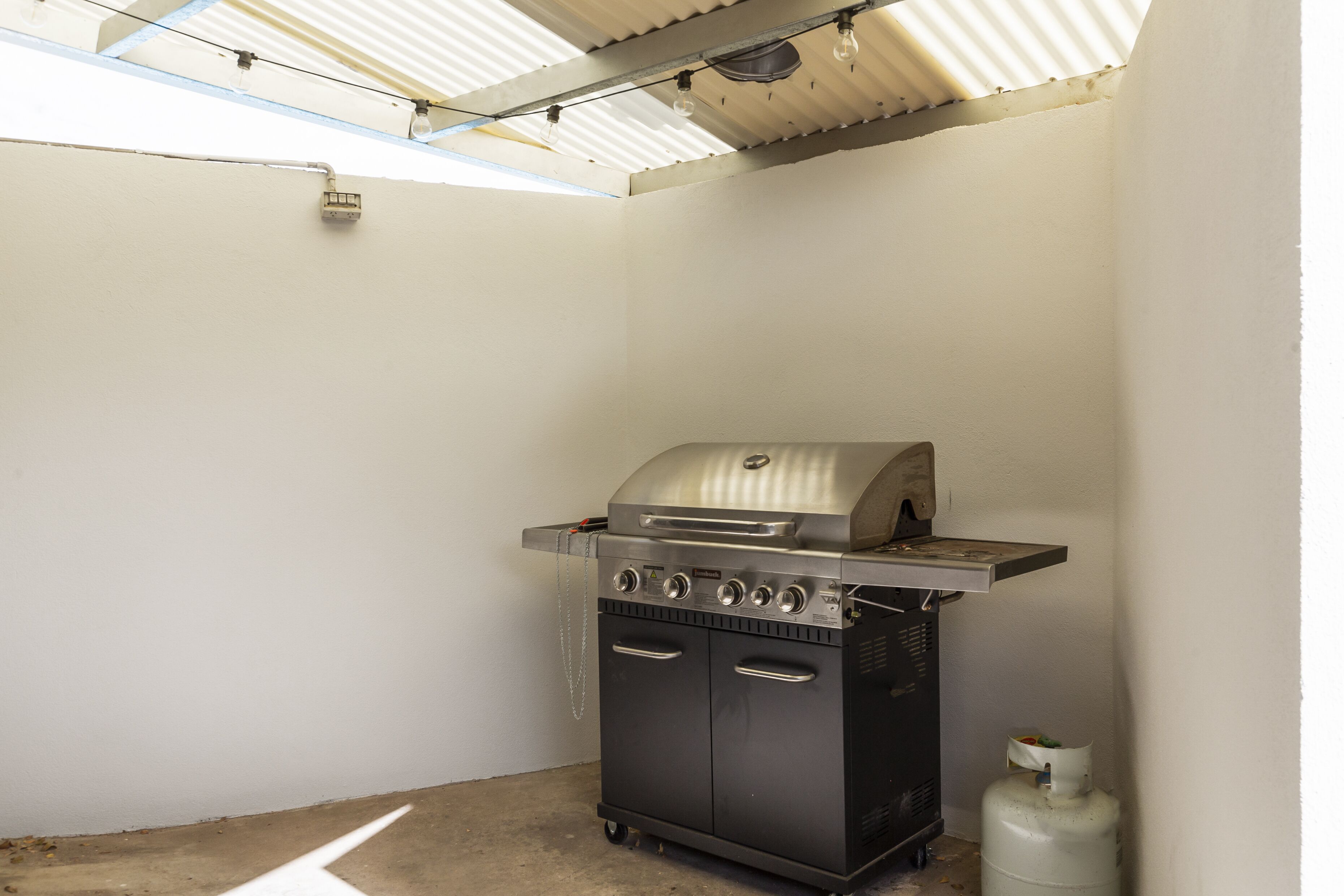 A compact, modern kitchen with a built-in gas grill, a gas tank, and a small countertop.