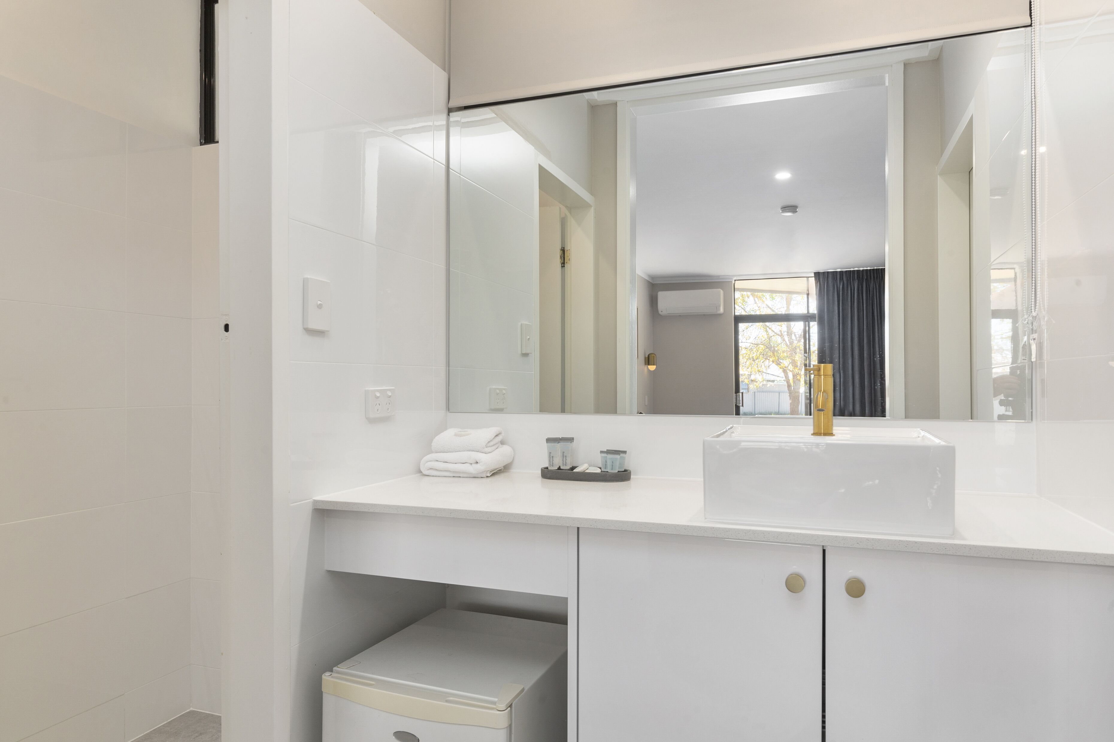 Un baño moderno con tocador blanco, un espejo grande y grifo dorado.