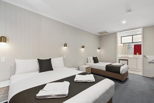 A hotel room with two beds, a small bedside table, a built-in wardrobe, and a bathroom with a red curtain.